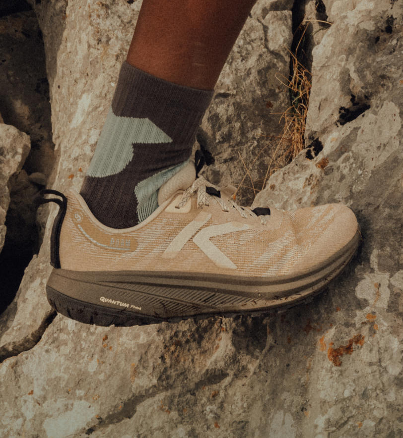 Knee-down shot of woman wearing Roam running shoes and traveling across a large rock.