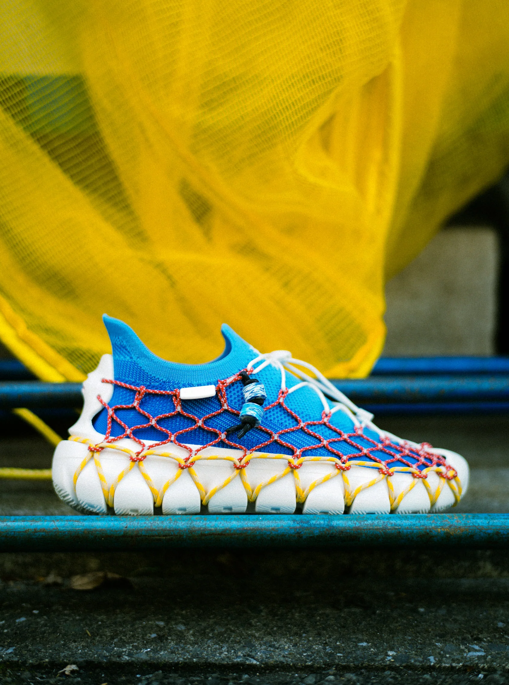 Product shot of the "Space Available" collaboration Uneek 360 Sneakers in blue and white, detailed with red and yellow lacing.